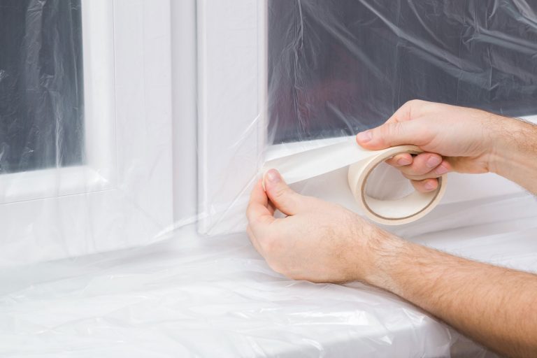 Worker putting tape on the cellophane, How To Insulate Windows With Plastic
