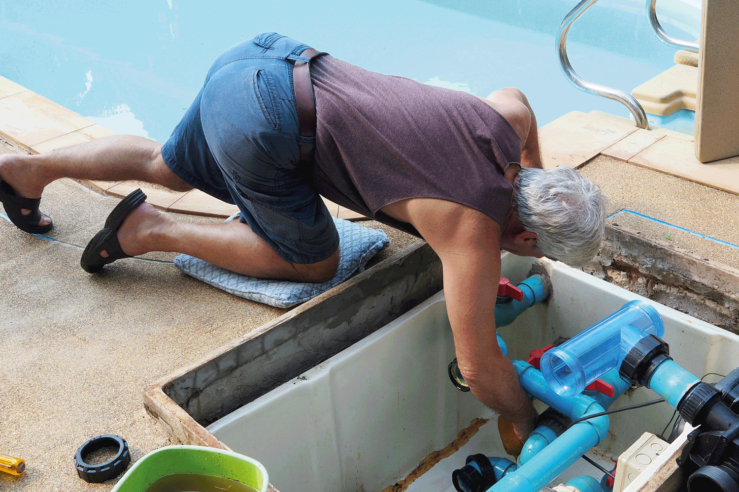 worker in comfortable summer wear peeking into the pool pump for maintenance
