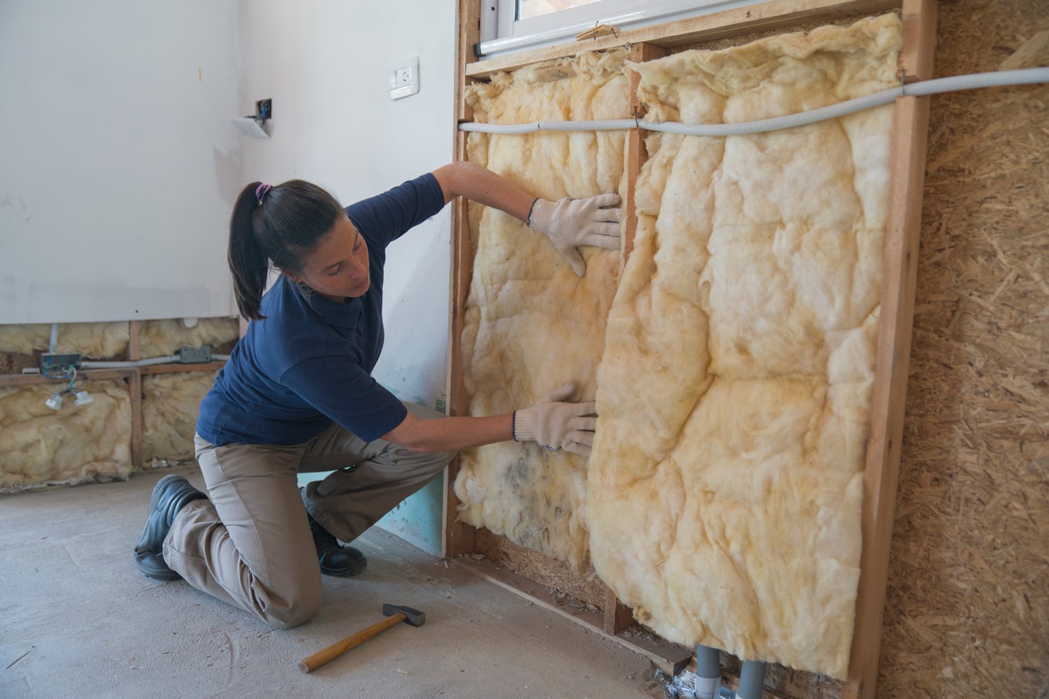 A female worker is installing a fiberglass insulation on a wall during wood frame house construction