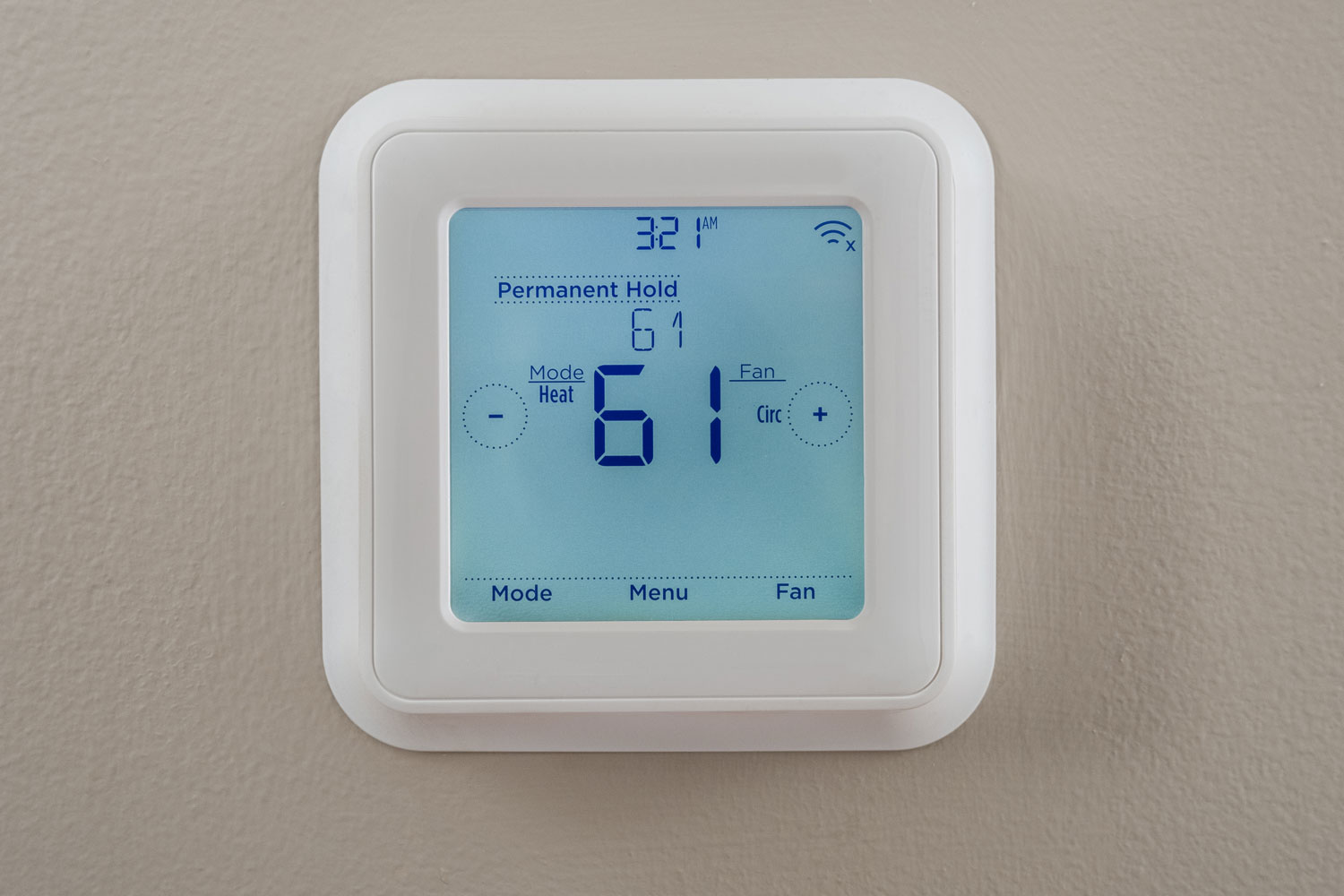 A thermostat mounted on the wall set at 61 degrees