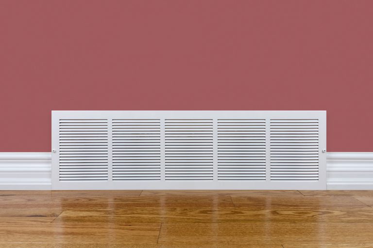 A white air vent inside a light red colored living room with wooden flooring, Where Should HVAC Vents Be Placed?