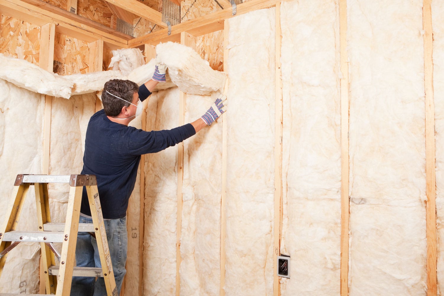 A worker placing mineral insulation between for the framing