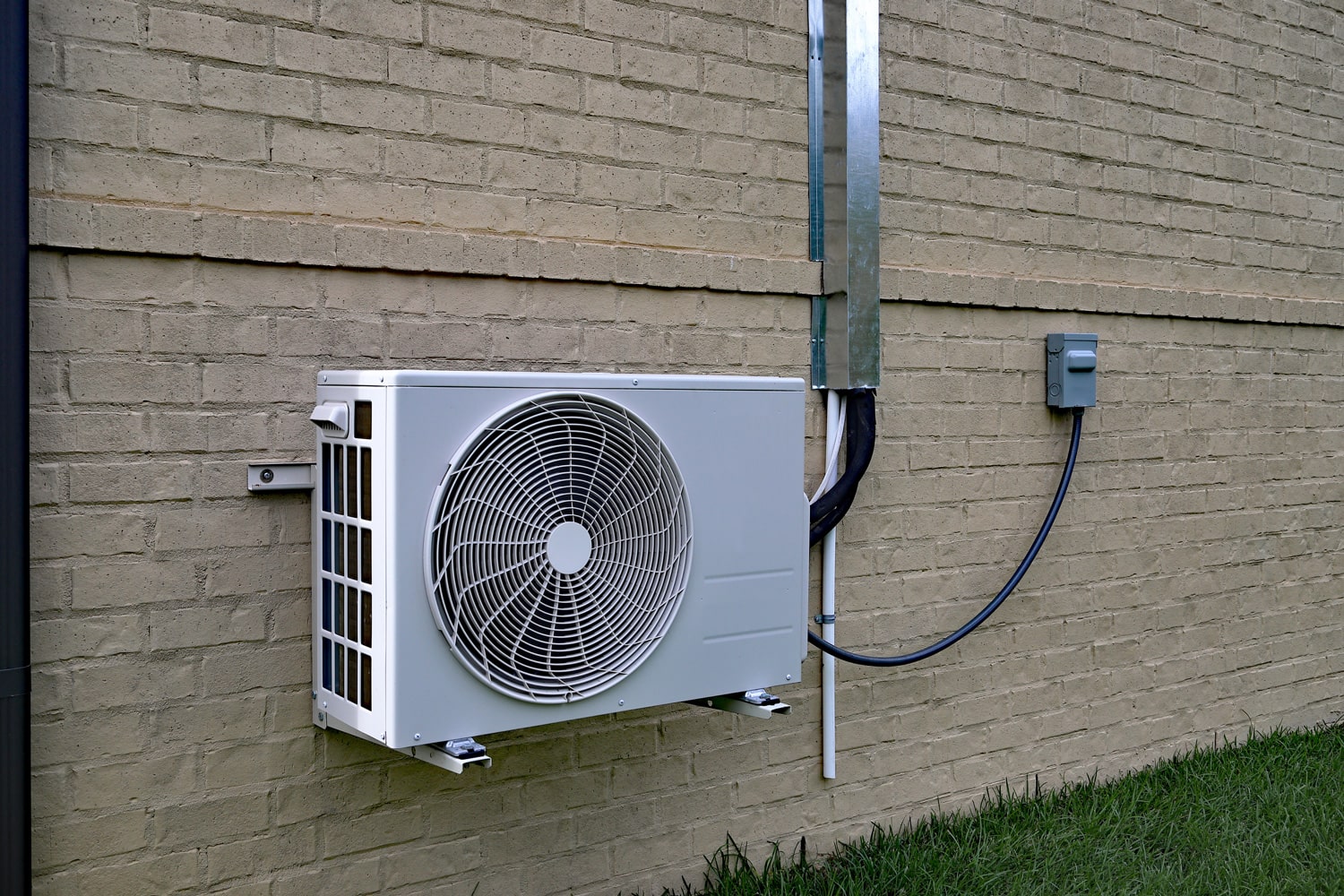 Air Conditioner mini split system next to home with painted brick wall 