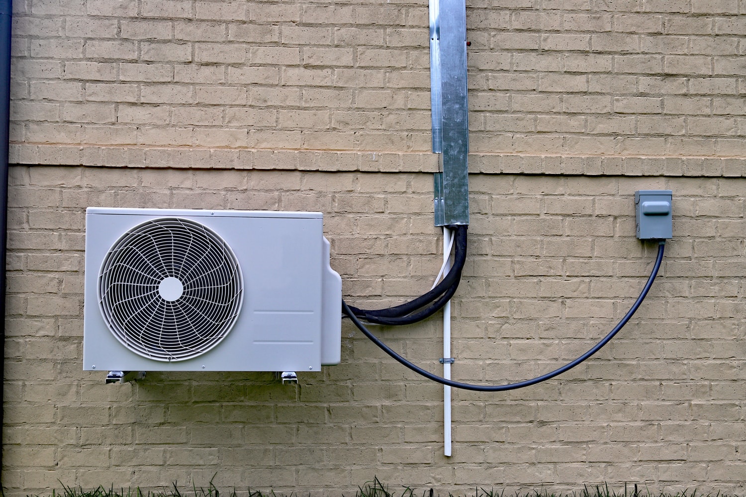 Air Conditioner mini split system next to home with painted brick wall
