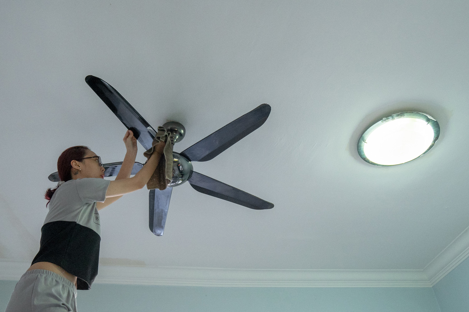An Asian woman cleaning ceiling fan at home.