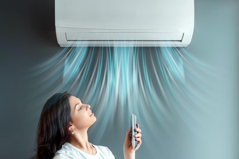 A beautiful girl stands under air conditioning and a stream of fresh cold air against a gray wall, How Long Should My AC Take To Cool [7 Factors To Consider]