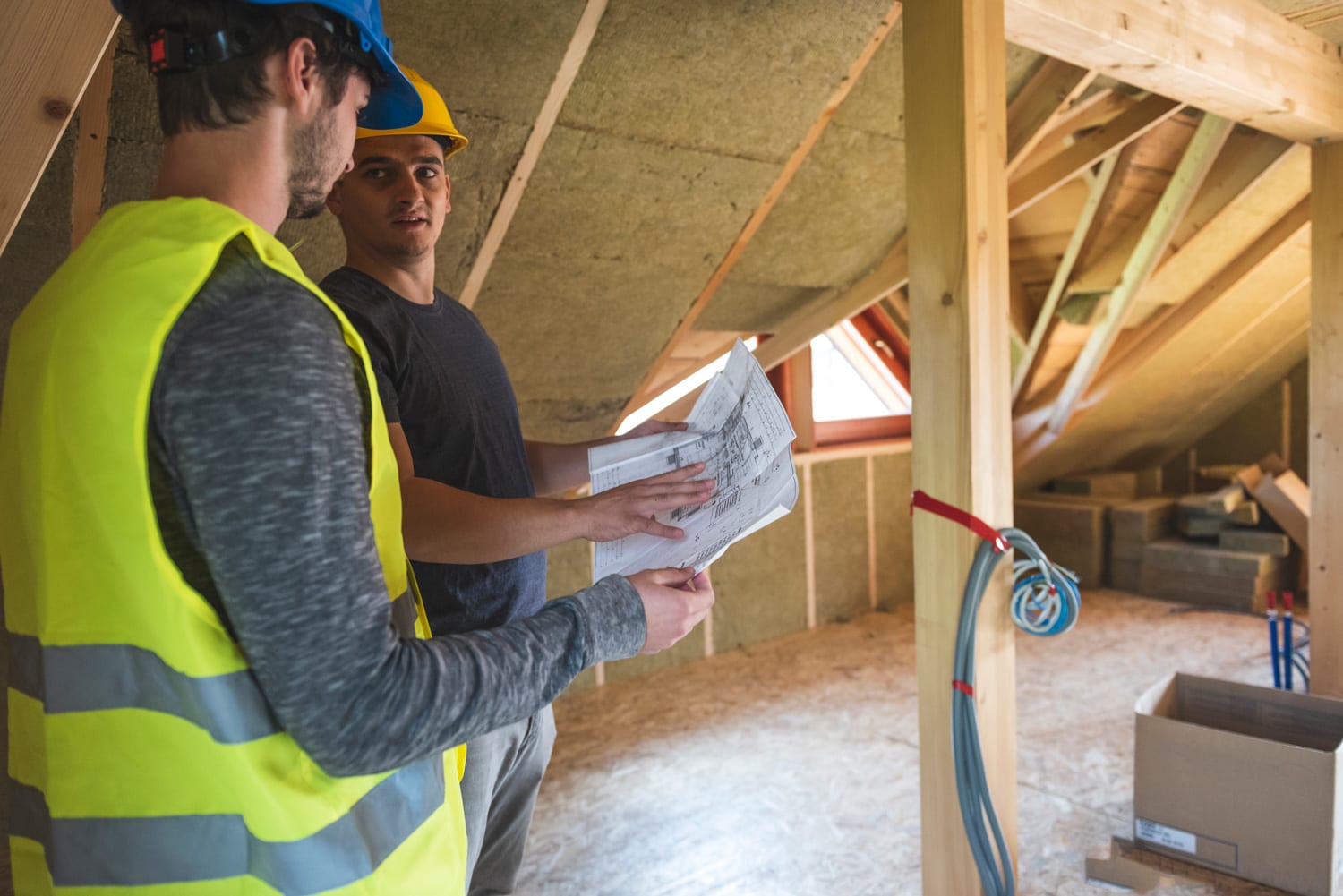 Construction workers reviewing blueprint at construction site.Roof with mineral rockwool in wall section. House under construction with insulation glass wool on an attic floor
