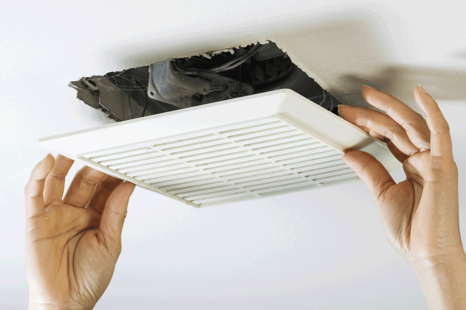 Close up horizontal photo of female hands removing bathroom fan vent cover from ceiling