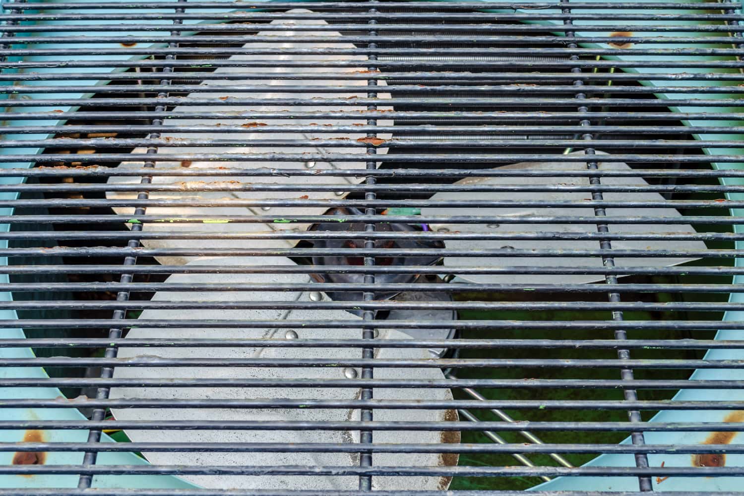 Close-up of a blue exterior residential air conditioner condensor with a rusty black grill