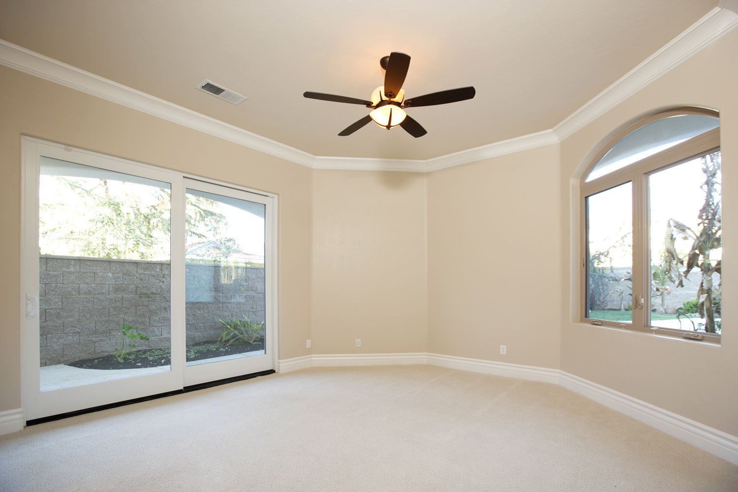 Empty room with tan walls, white trims, sliding doors and windows with a ceiling fan