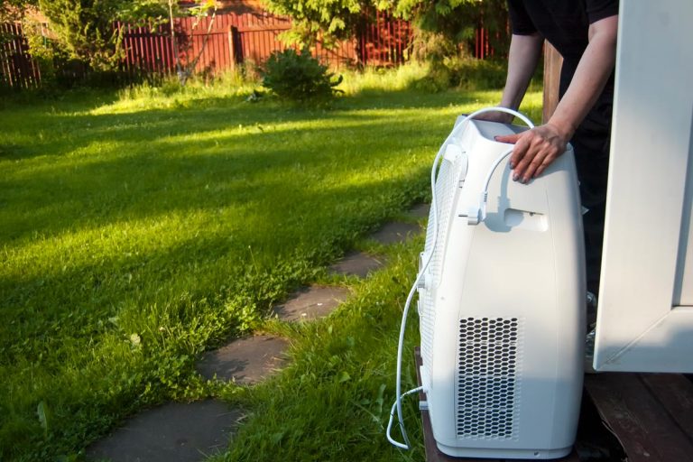 A female hands moving a portable air conditioner into a house, How Often Should You Drain A Portable Air Conditioner?