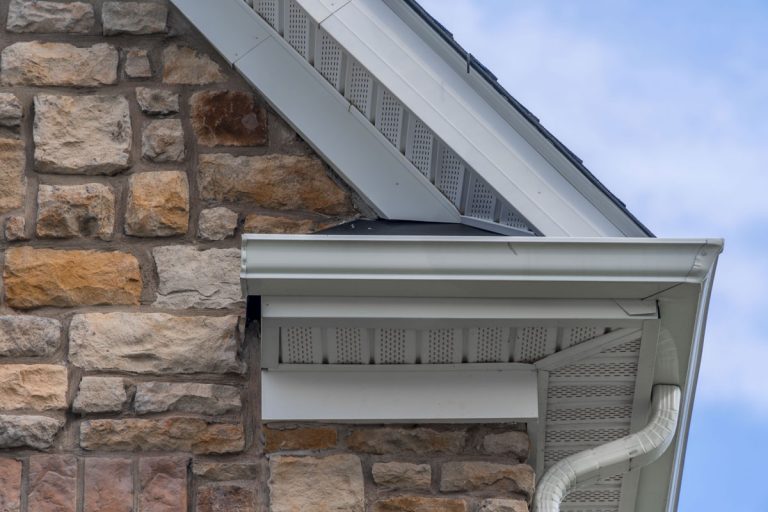 Gable with colored stone siding, white frame gutter guard system, fascia, drip edge, soffit, on a pitched roof attic, Can You Install A Soffit Without Fascia?
