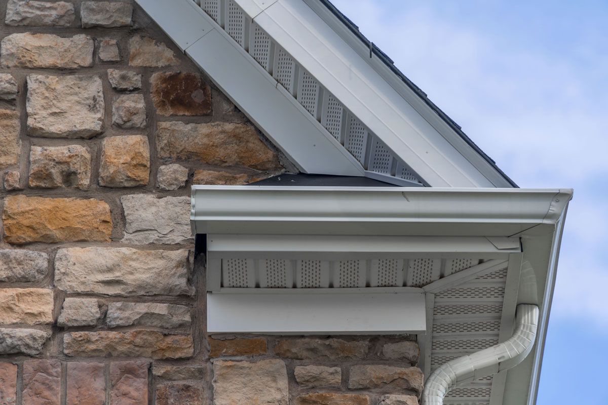 Gable with colored stone siding, white frame gutter guard system, fascia, drip edge, soffit, on a pitched roof attic