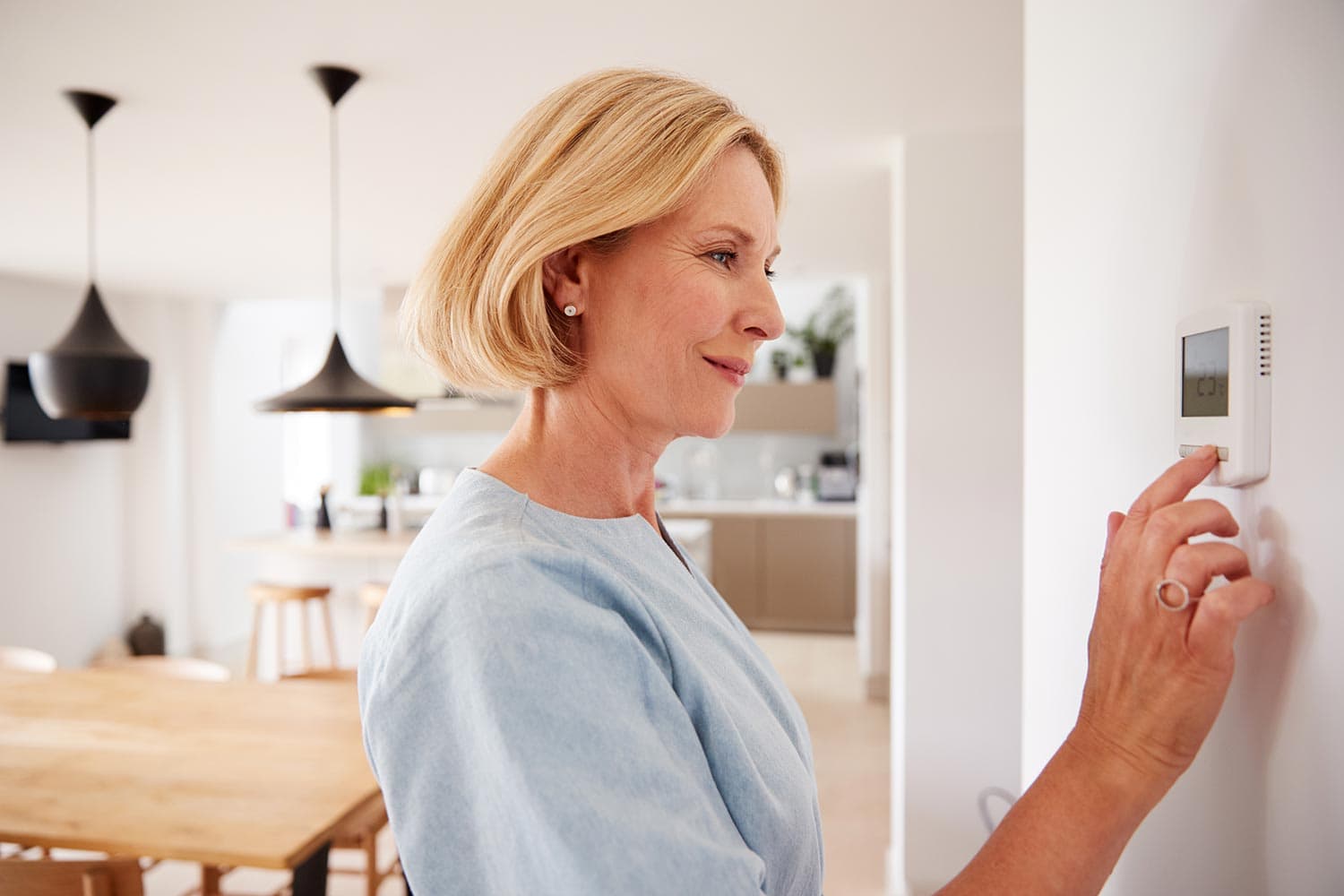 Mature woman adjusting central heating temperature at home on thermostat