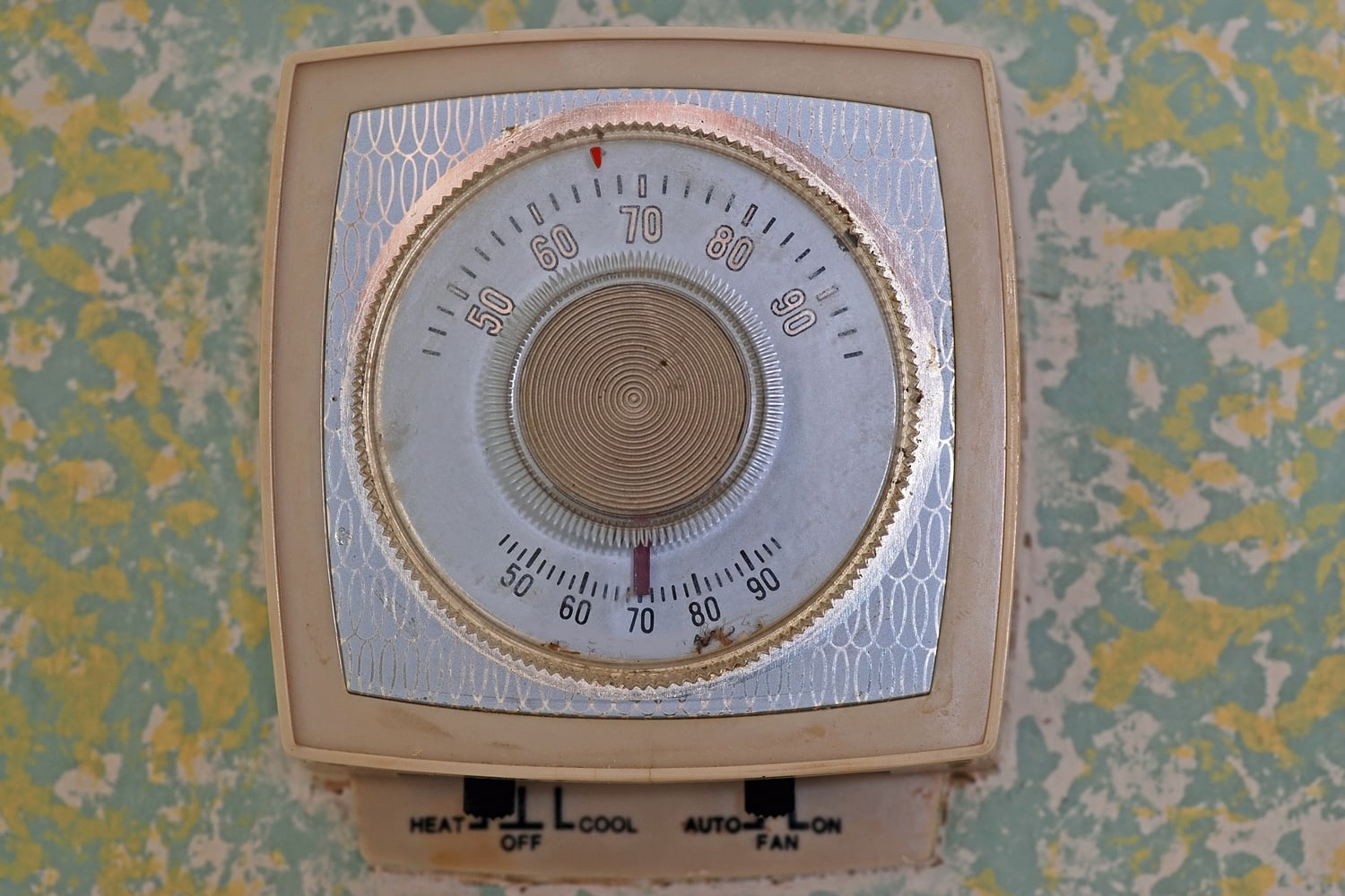 Old home temperature control unit on colorful wall -- dirty and grungy, indicating age - Thermostat Won't Go Above 70 - What To Do