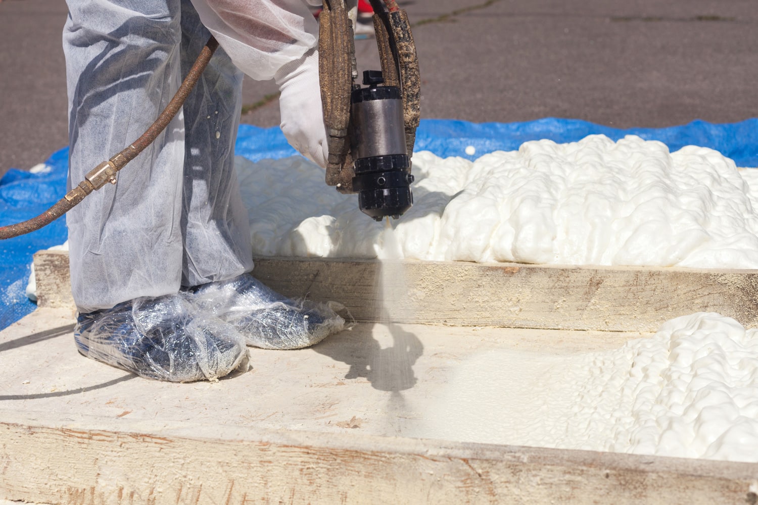 Technician dressed in a protective white uniform spraying foam insulation using Plural Component Spray Gun.