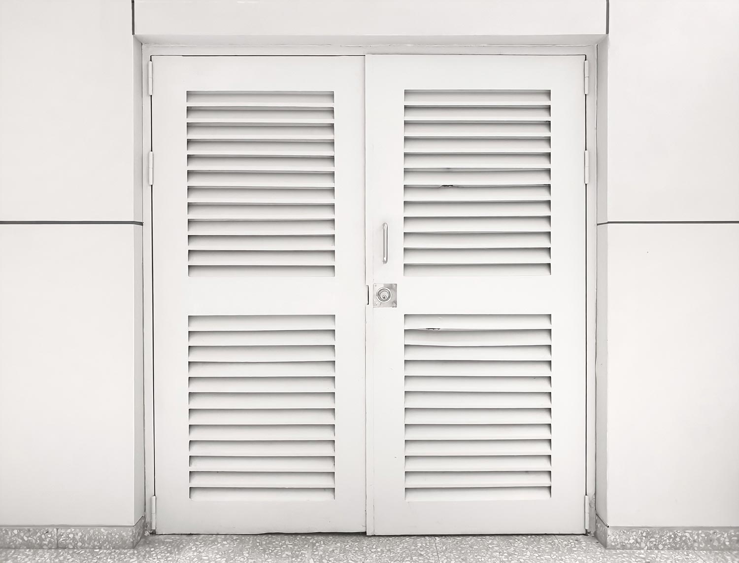 The louver wooden white door is locked with the white wall