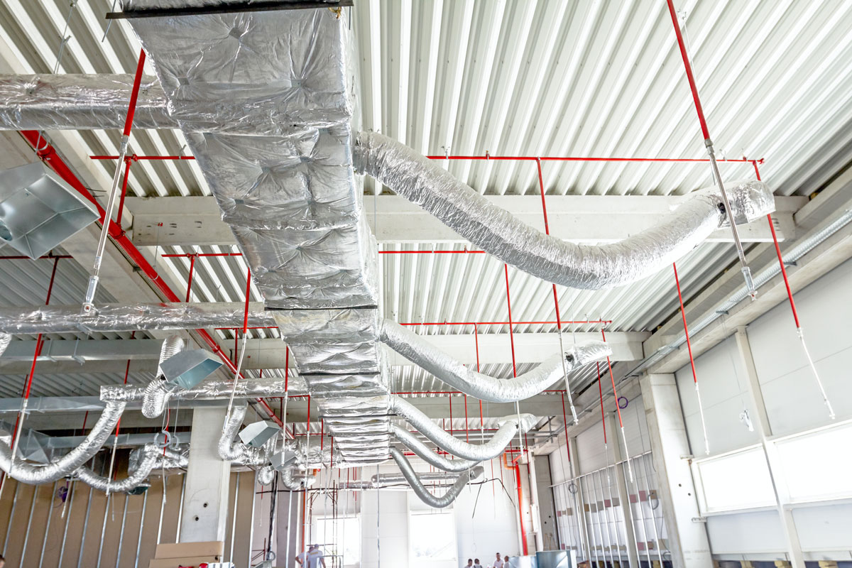 Ventilation pipes in silver insulation material and fire sprinkler on red pipe are hanging in the ceiling