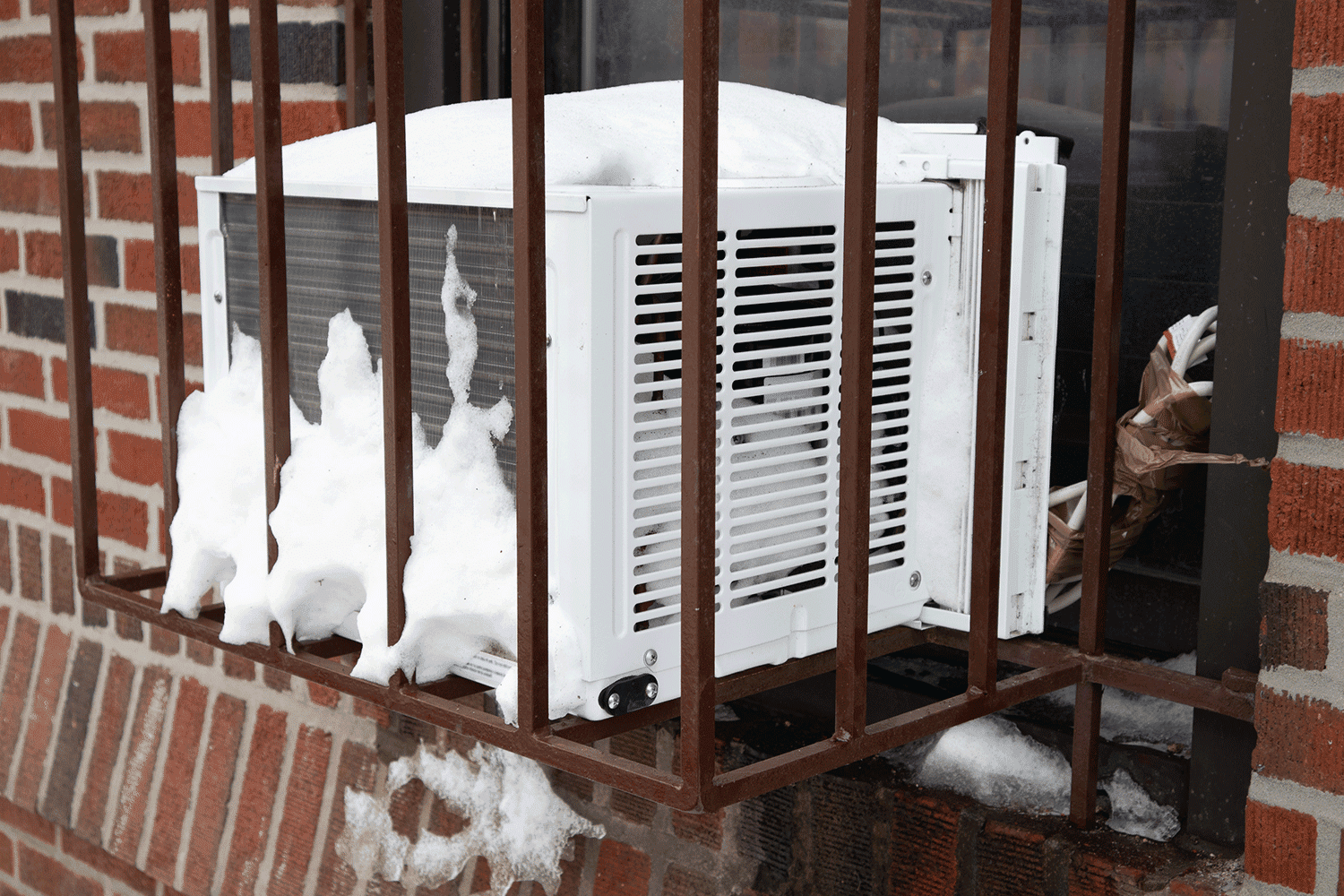 Window air conditioner in a barred cage with snow