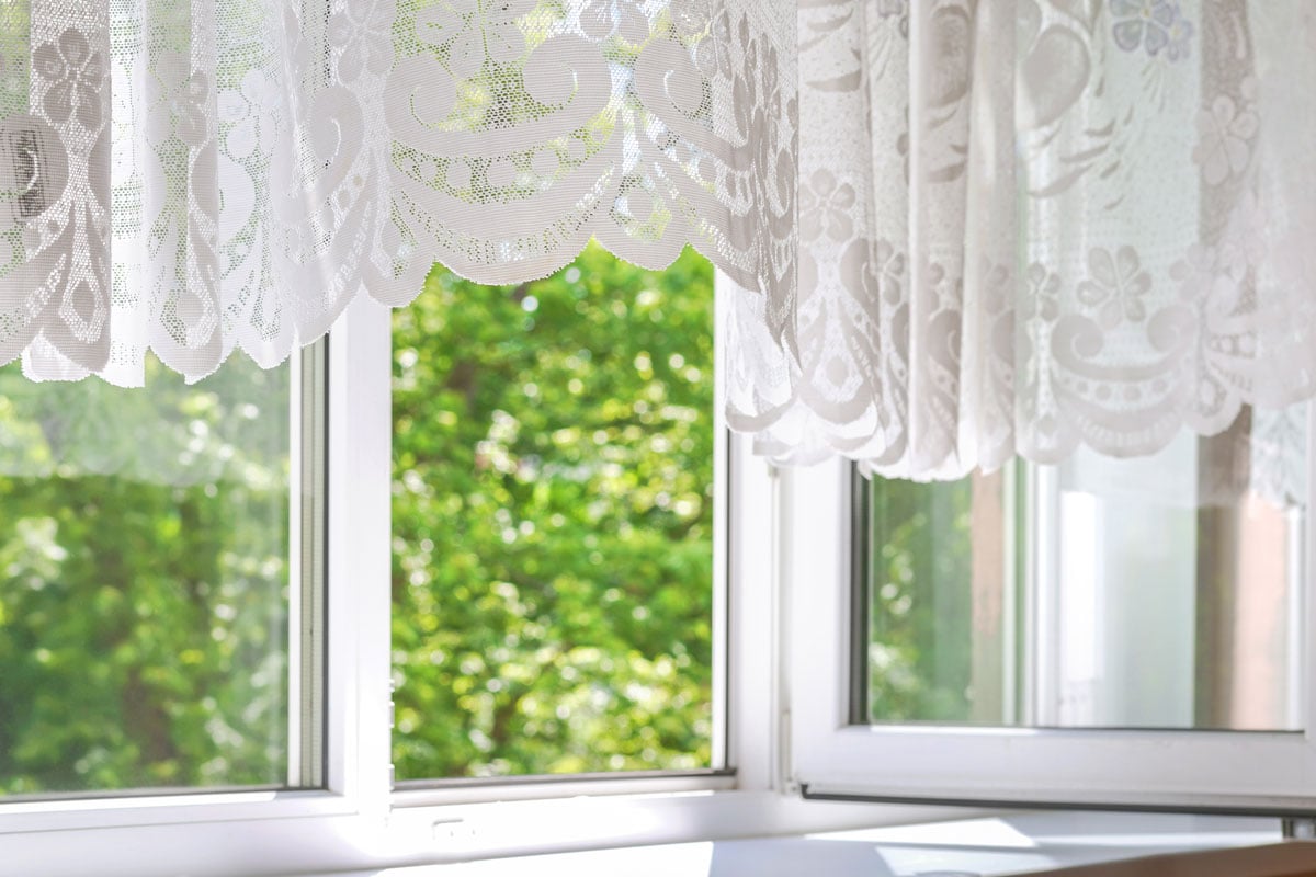 Windows with lacy curtains with green garden tress under a sunlight on summer day