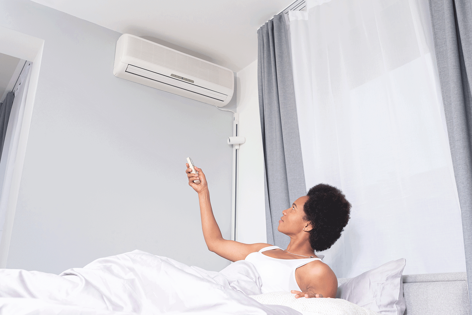 Woman switching on air conditioner lying in bed at home