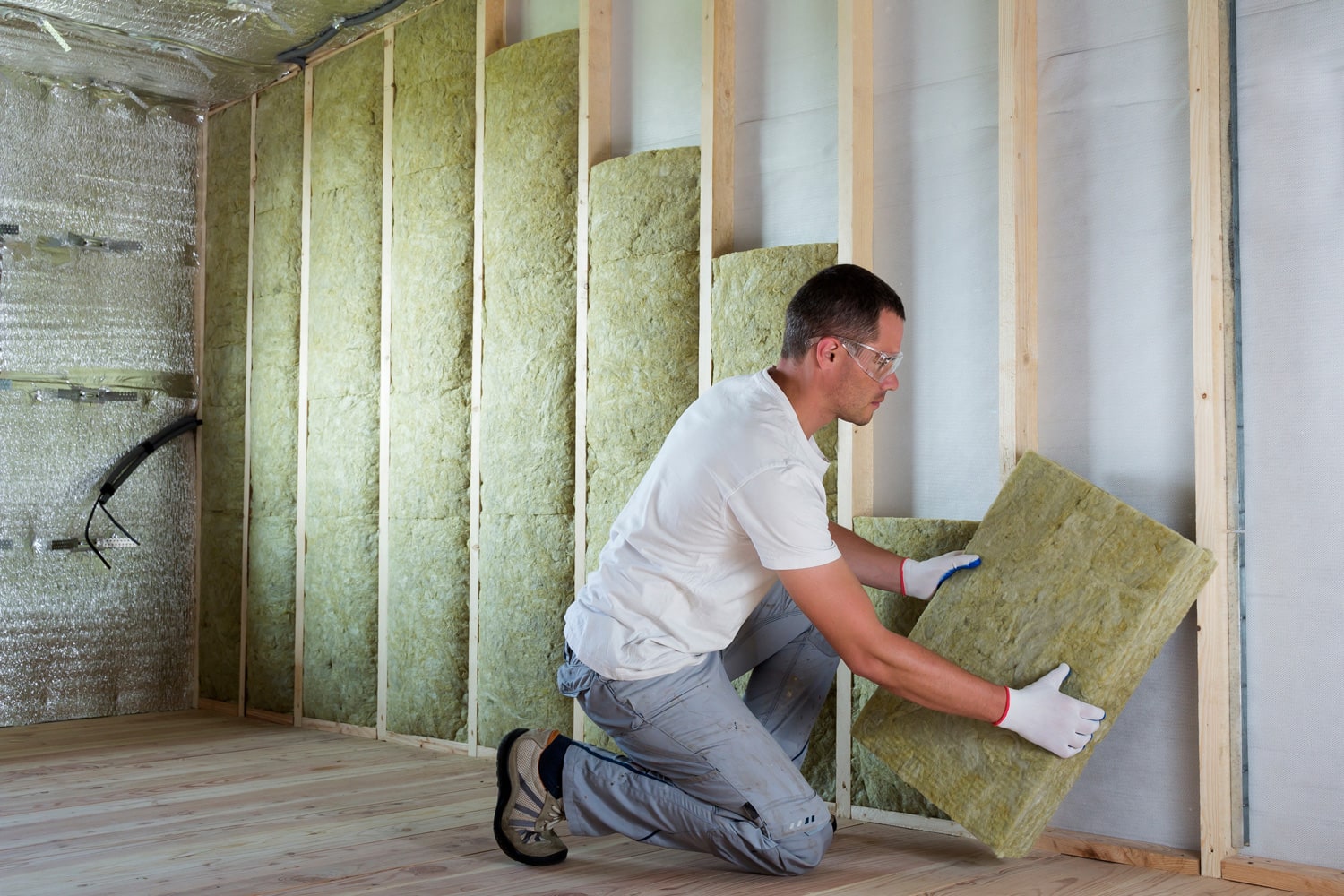 Worker in protective goggles and respirator insulating rock wool insulation in wooden frame for future house walls for cold barrier.