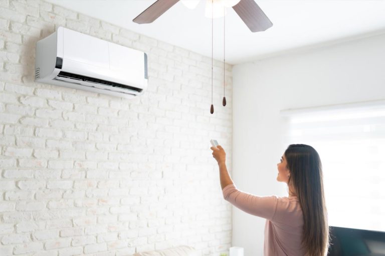 A young woman adjusting temperature of air conditioner using remote control, Can One Mini Split Cool Multiple Rooms?