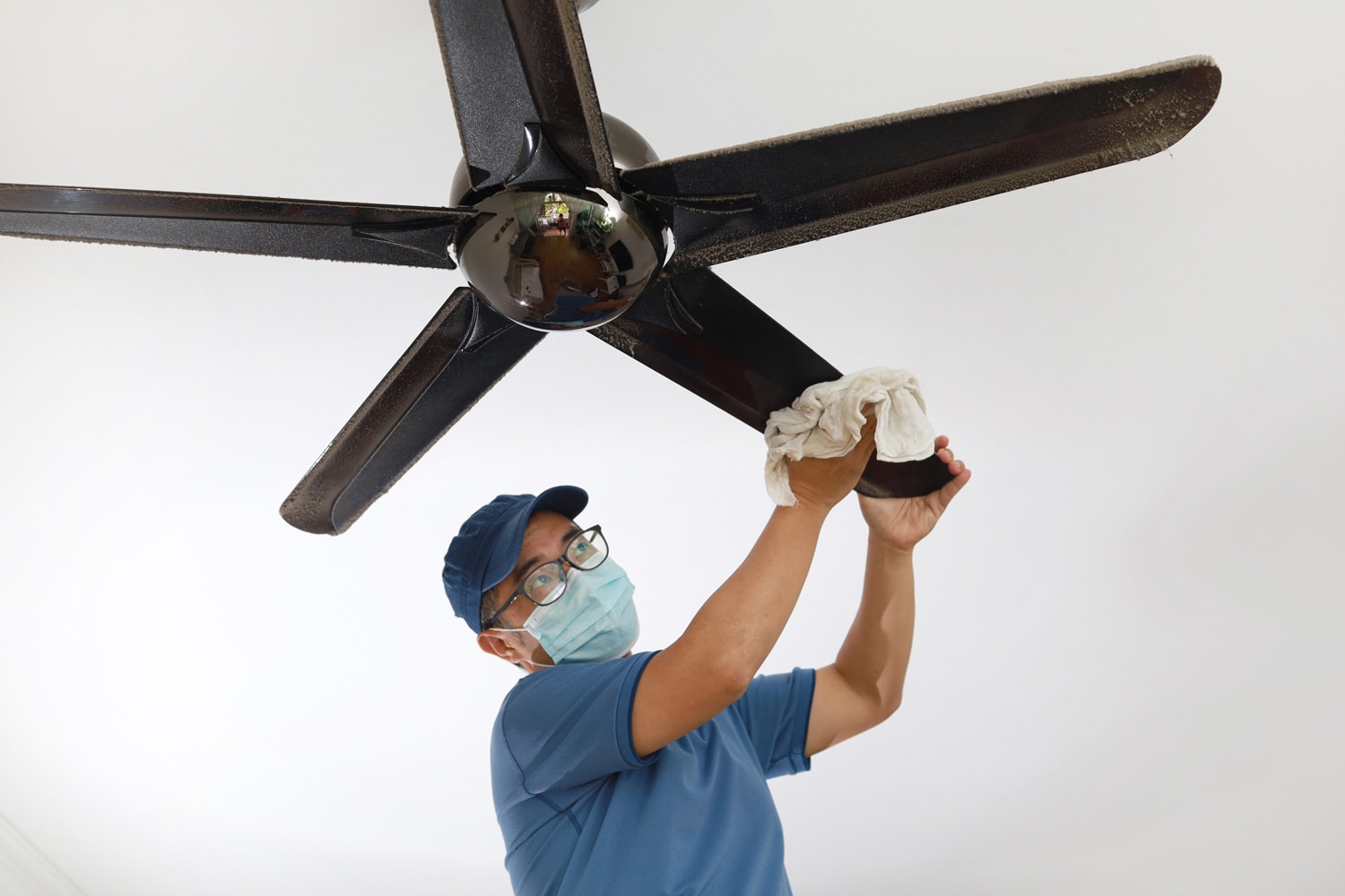  man wearing a protective mask cleaning ceiling fan at home