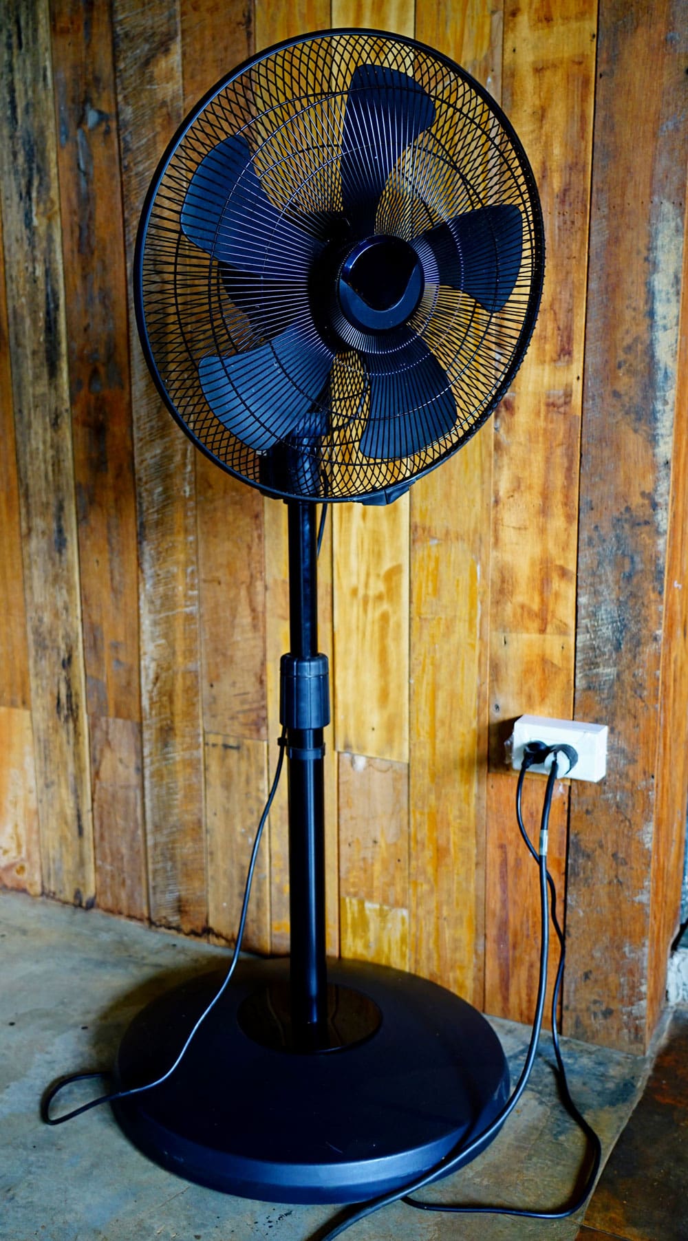 A black stand fan plugged into the wall