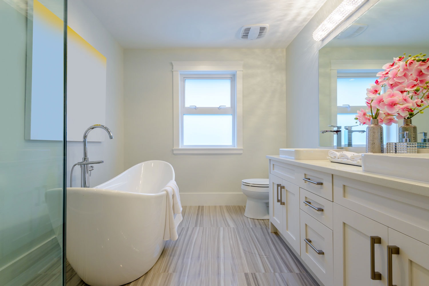 A boat shaped bathtub inside a modern bathroom with laminated flooring, white walls and a white awning window