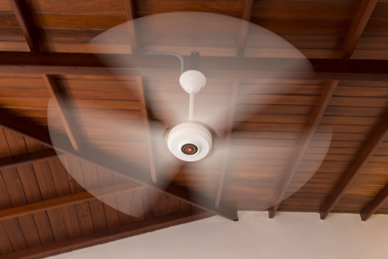 A white spinning electric fan inside a rustic wooden room