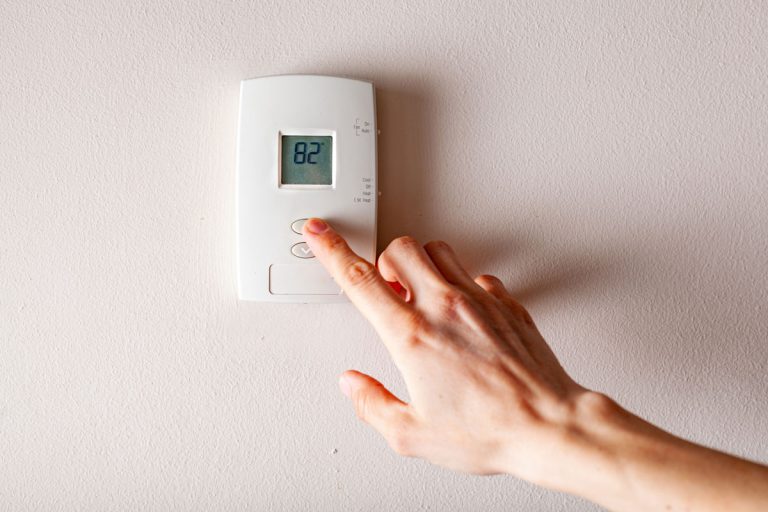 A woman is pressing the up button of a wall attached house thermostat with digital display showing the temperature,Will A Bad Thermostat Cause AC To Freeze Up?