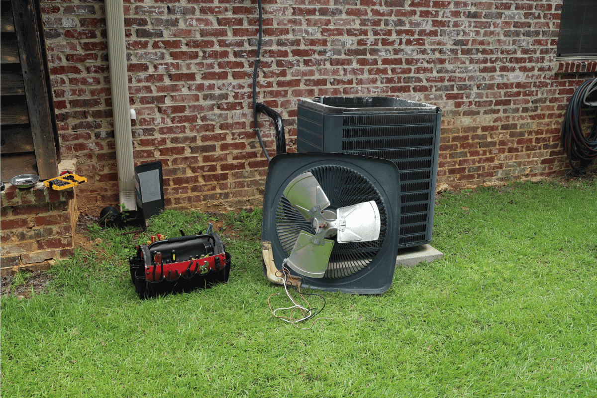 Air Conditioner compressor condenser coil with fan and tools being worked on next to a brick house for repair maintenance. How To Reset A Ruud Air Conditioner