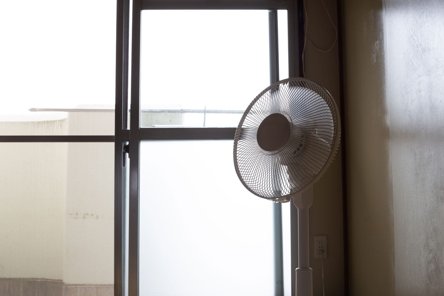 An electric stand fan placed on the corner of the room
