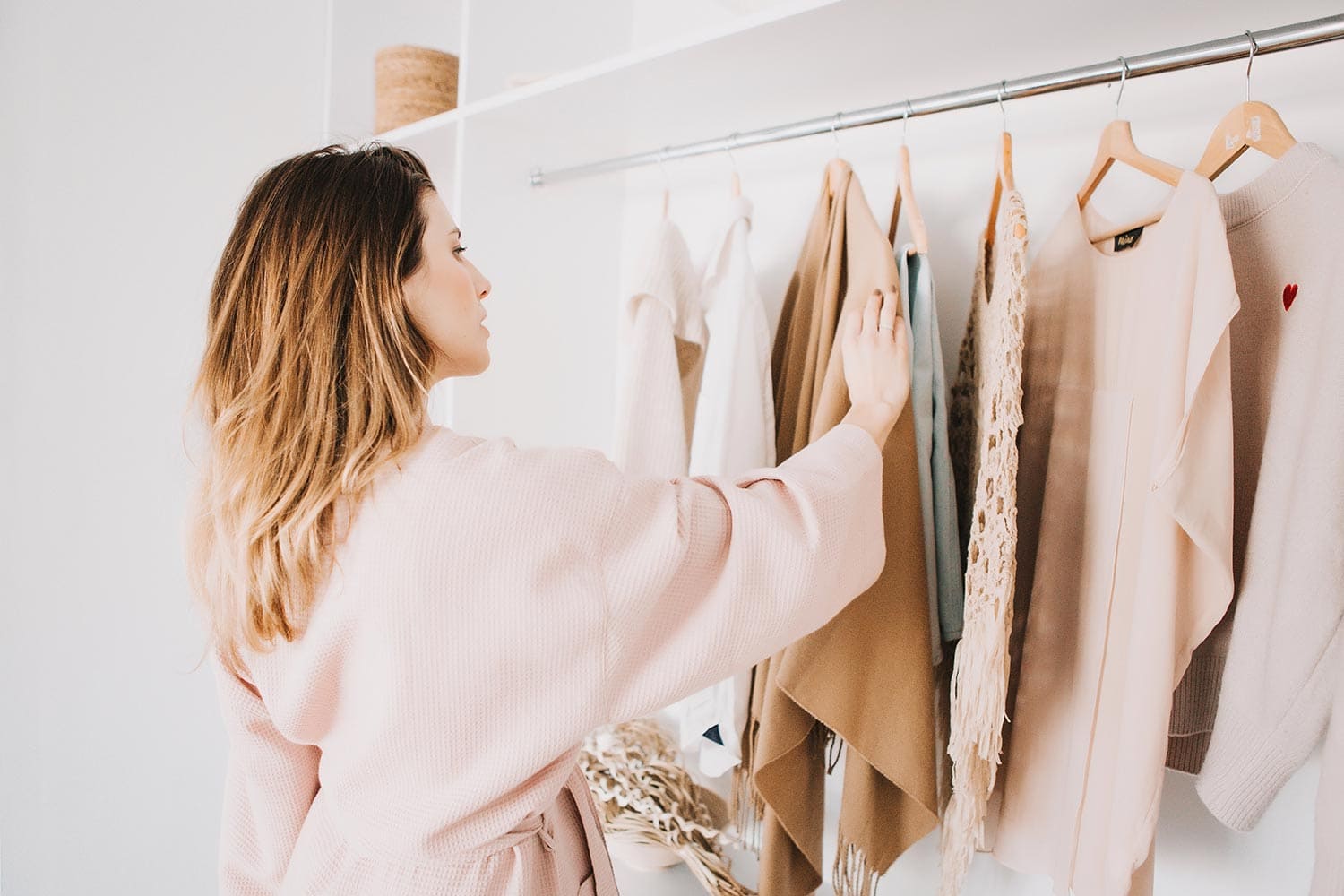 Cute young woman in bathrobe standing in front of hanger rack and trying to choose outfit dressing for work or walk