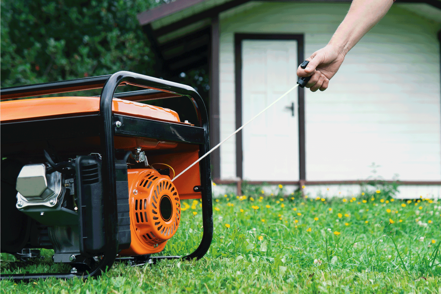 Female hand starts a portable electric generator standing on the grass in front of a summer house in summer evening