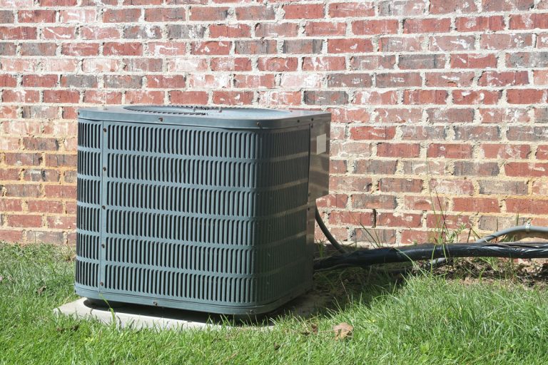 Home Air Conditioner Condenser coil sitting in front of brick wall, AC Pro Vs. Lennox: Which Is Better? - Differences Explained