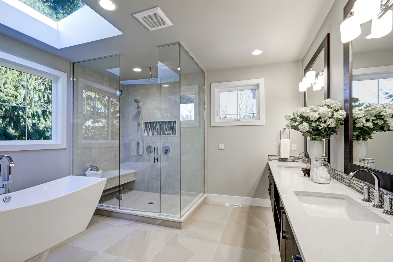 Luxurious and spacious modern bathroom with a glass walled shower area, light gray walls, and white casement windows