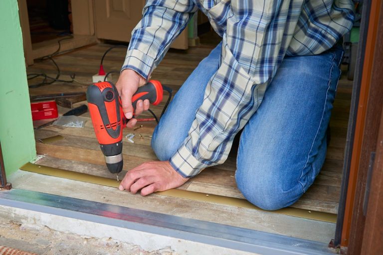 A man twists a threshold drill in the door, How To Seal An Exterior Door Threshold