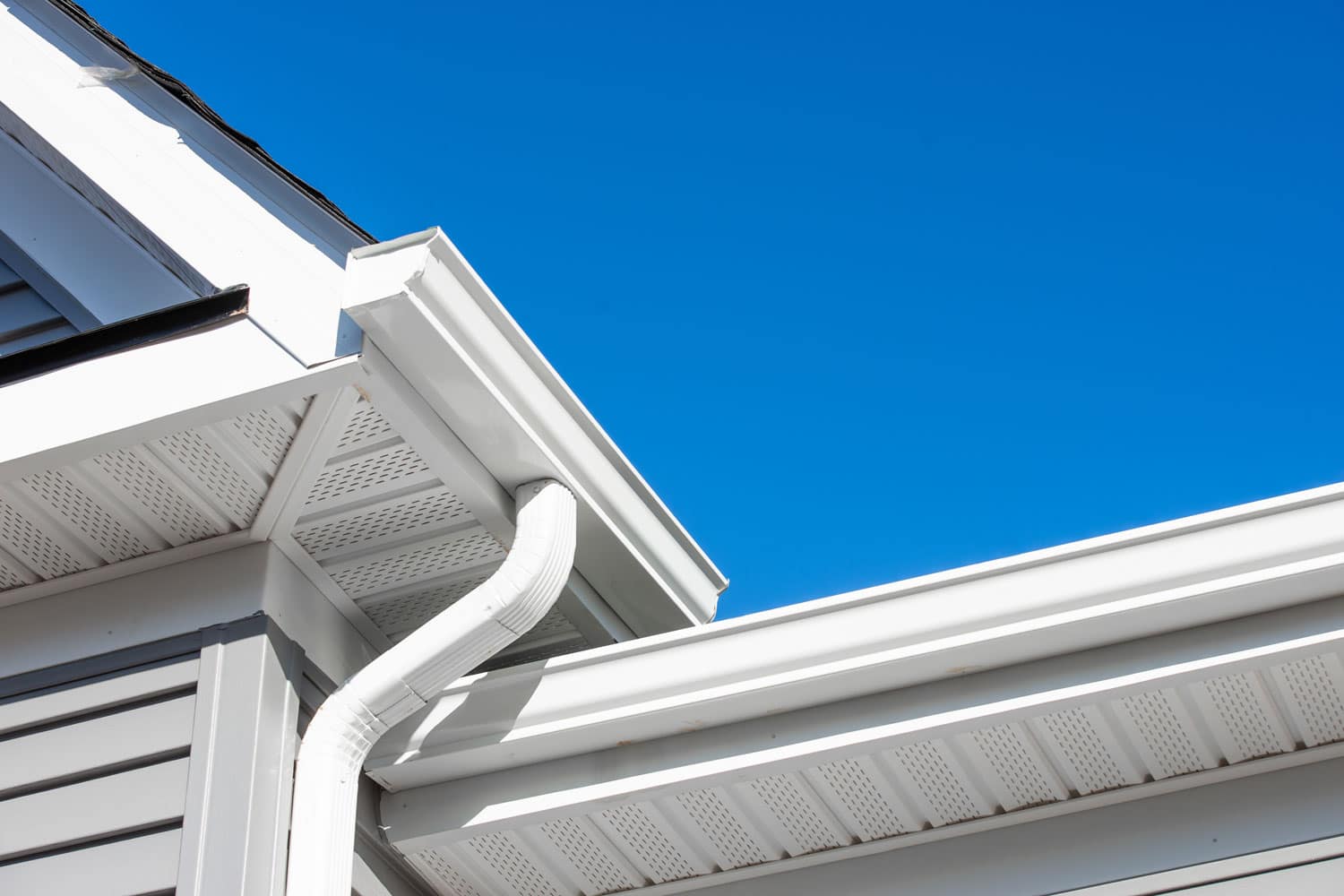 Metal gutters coated in white with a PVC downspoout and soffit installation