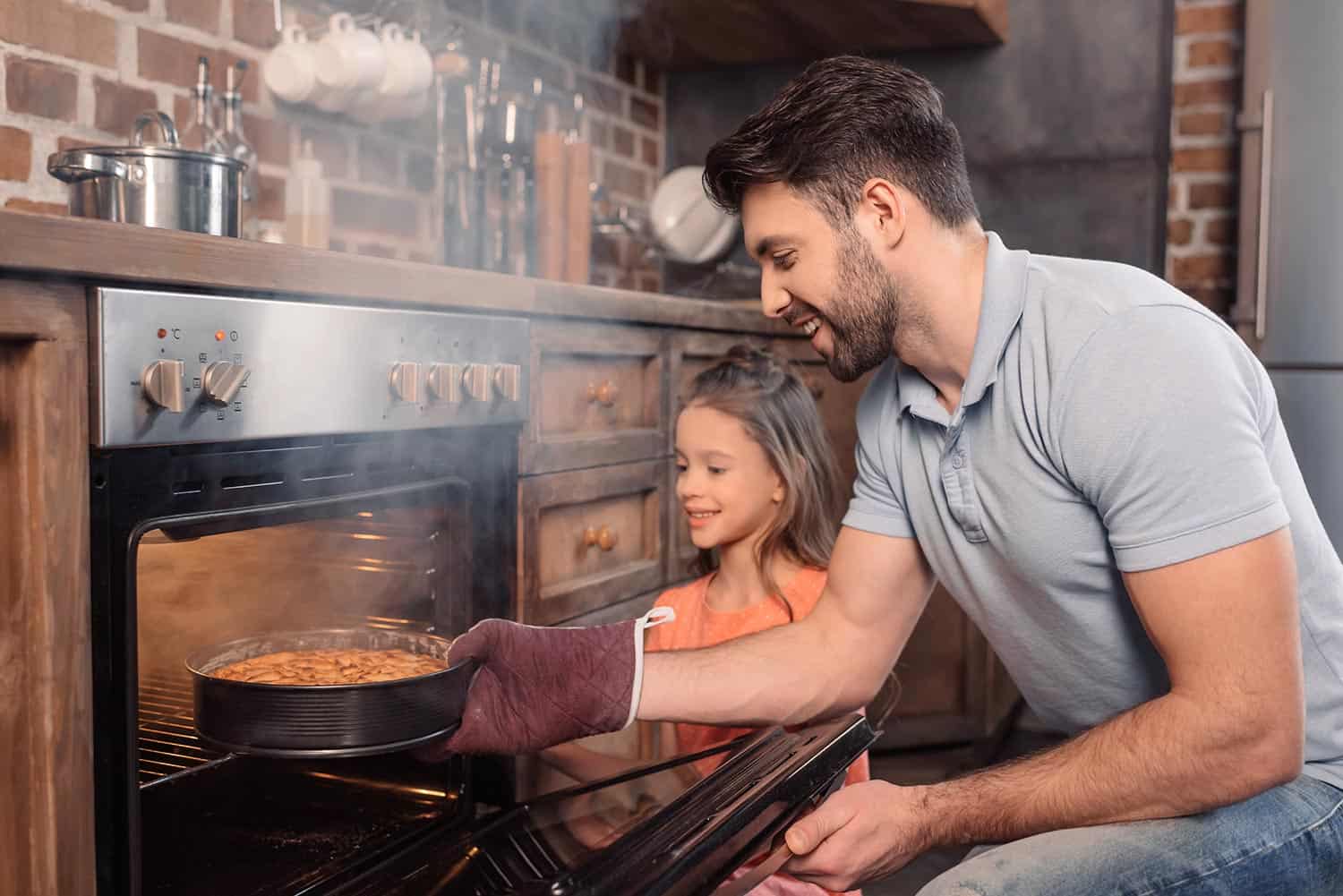 Smiling father and daughter taking cake from oven