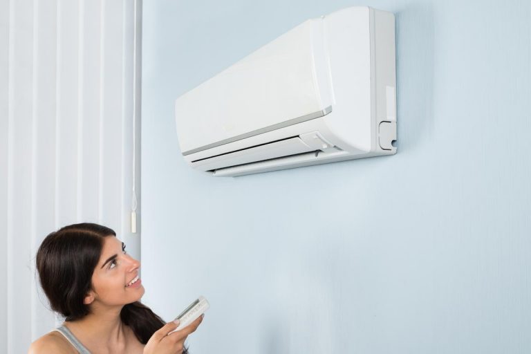 A woman holding remote control air conditioner in house, How Long Do Trane Air Conditioners Last