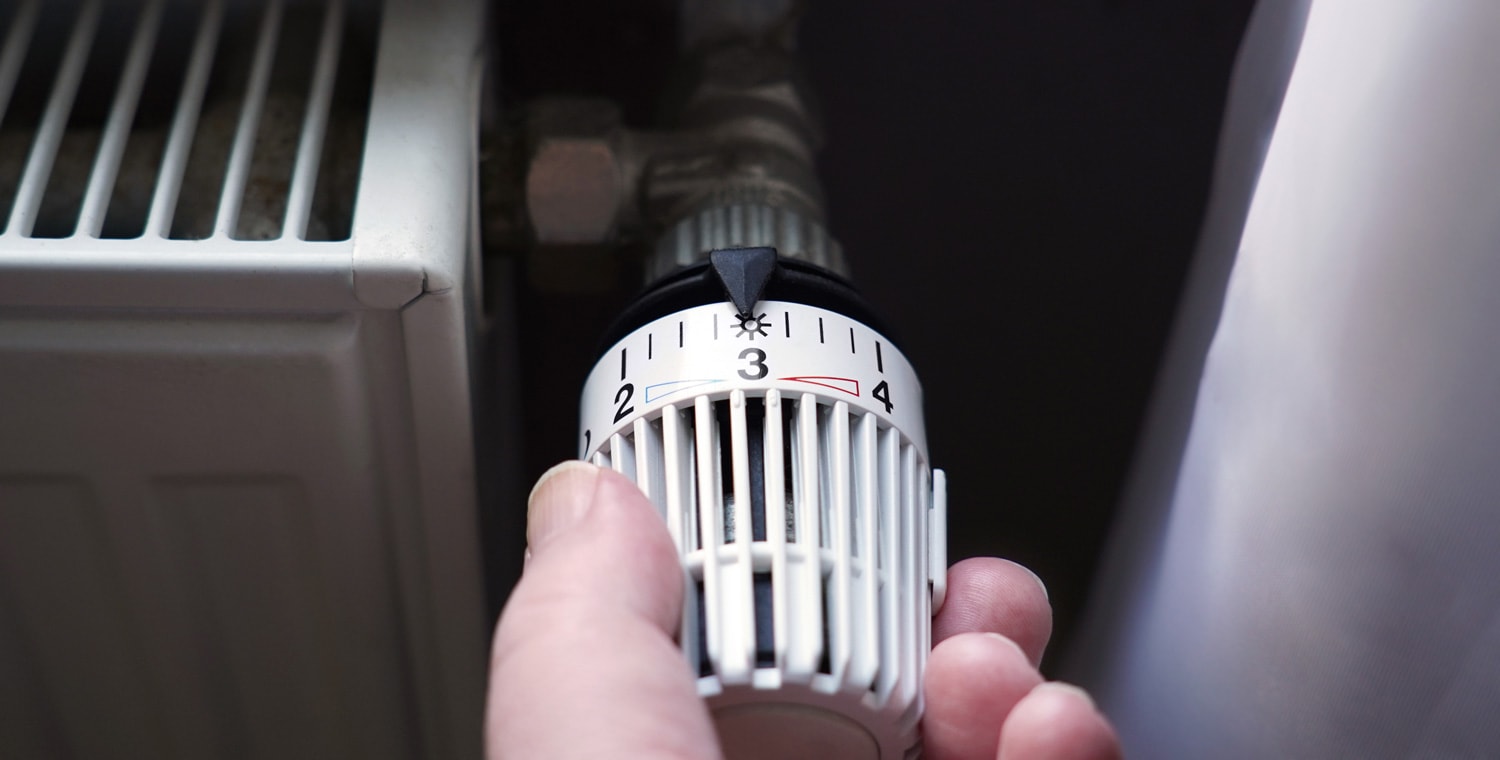 hand turning down thermostat on radiator to save energy due to heating cost price hike