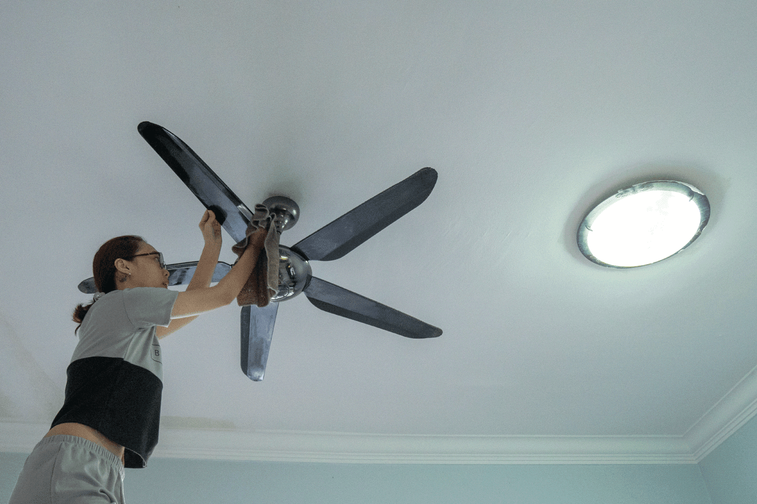 woman cleaning ceiling fan at home.