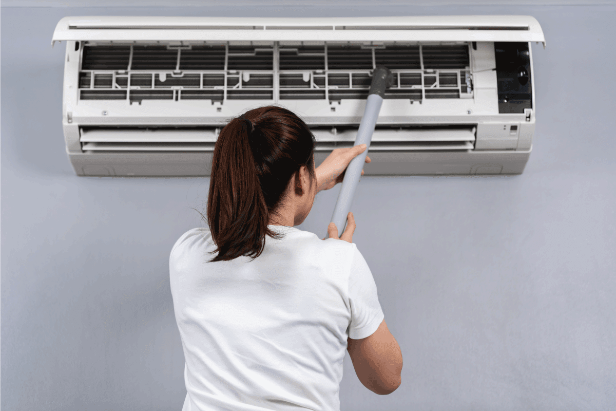 young woman using vacuum cleaner to cleaning the air conditioner at home. How To Reset Rheem AC Unit
