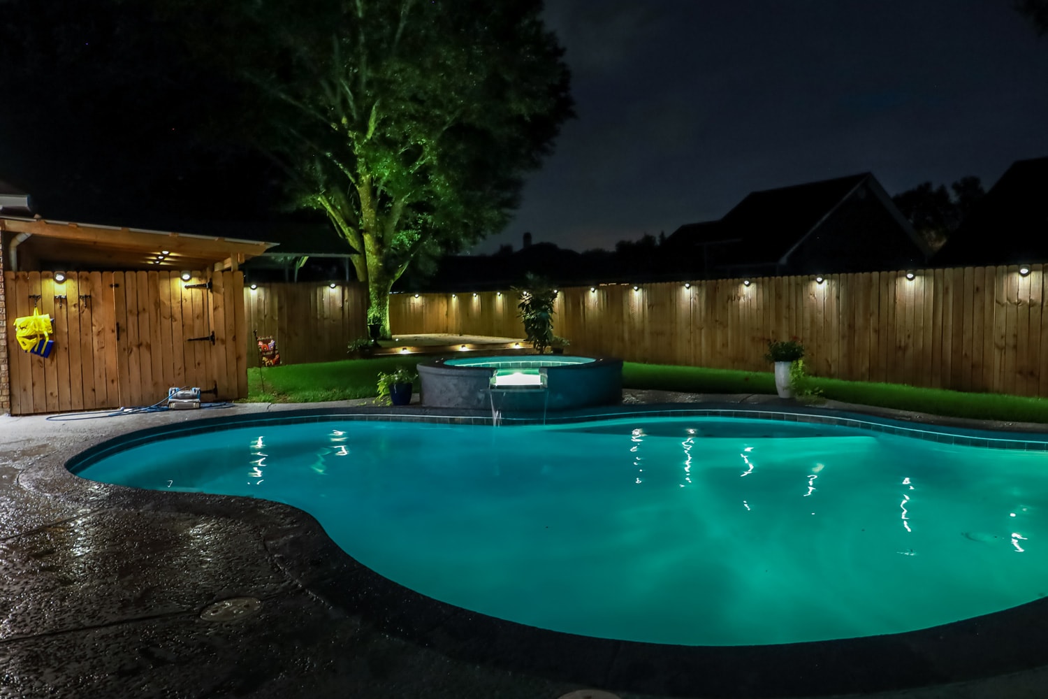A backyard swimming pool and Hot Tub hot tob at night with solar lights around the fence for privacy and illumination.