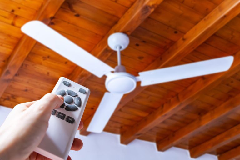 A person using a remote control to operate a ceiling fan mounted in a house on a wooden ceiling, How To Reset Minka Aire Fan Remote