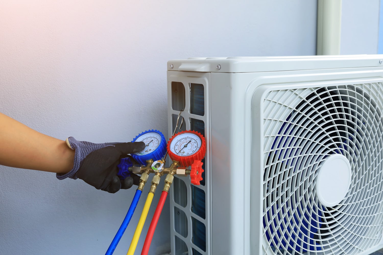 An air conditioner technician's serviceman hand holding a manifold gauge to check the pressure inside the system to normalize the refrigerant charge during high temperatures and hot weather. Maintain.