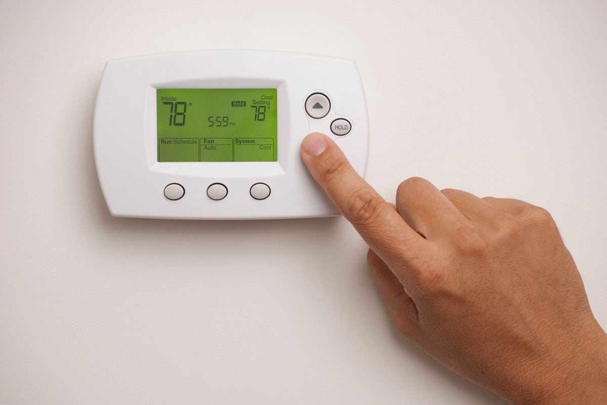 Digital Thermostat with a male hand, set to 78 degrees Fahrenheit
