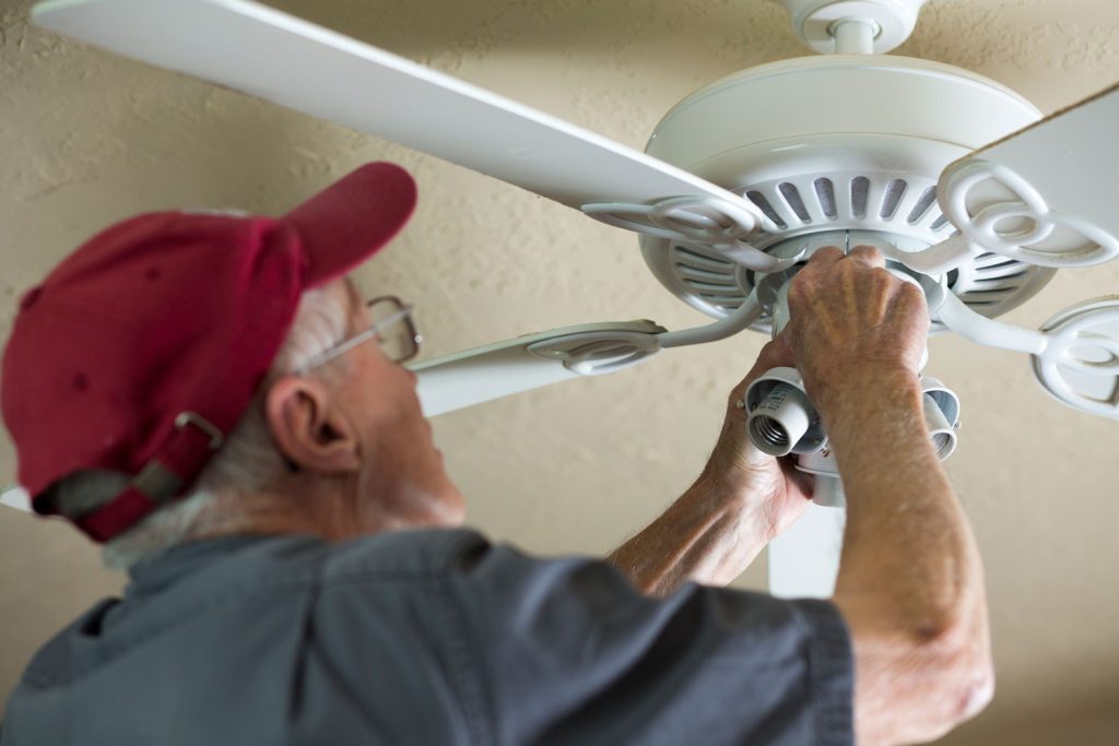Electrician repairing ceiling fan for neighbor. He replaced the motor for the fan. Blue collar Caucasian senior man is retired but is still active and enjoying doing small repairs for others. Helping neighbors.